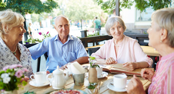 Senioren - ein Mann und dreit Frauen sitzen in einem Café am Tisch und unterhalten sich.